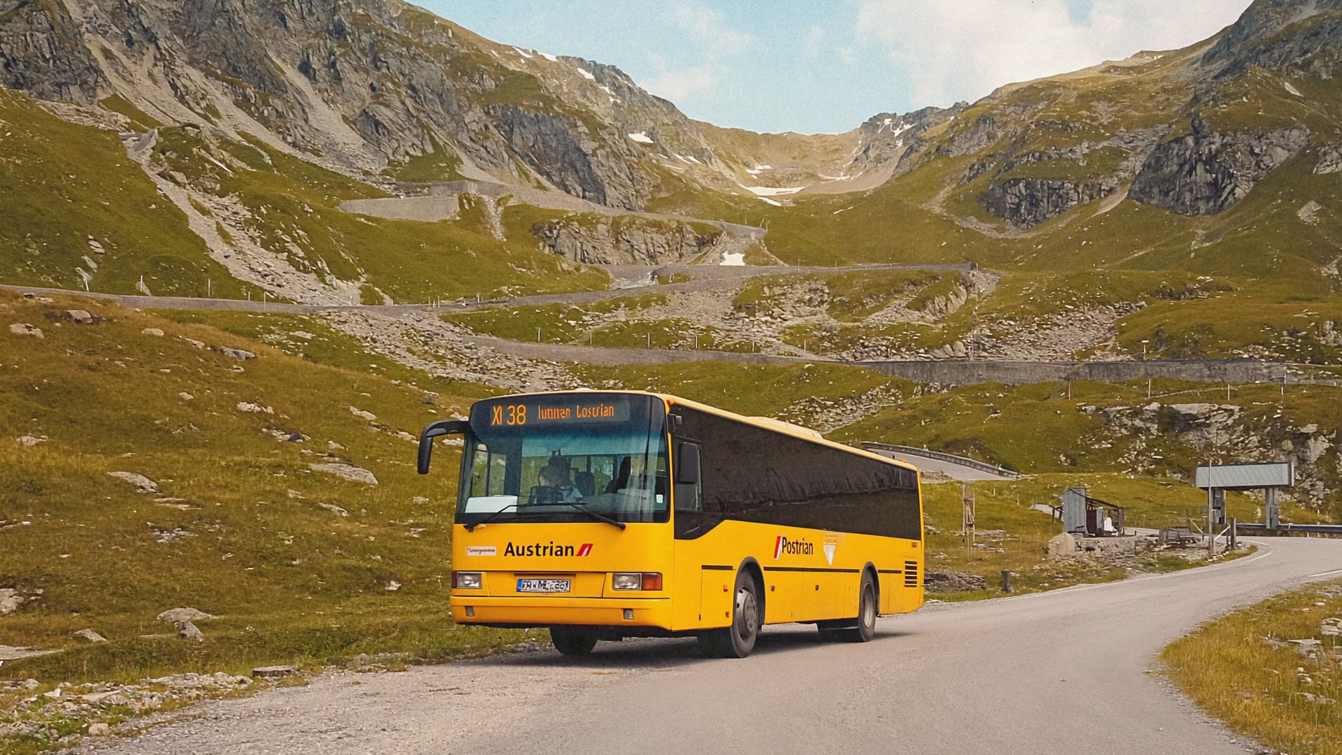 Ein gelber ÖBB-Postbus an einer alpinen Haltestelle, dahinter aufsteigende Berghänge in spätem Tageslicht